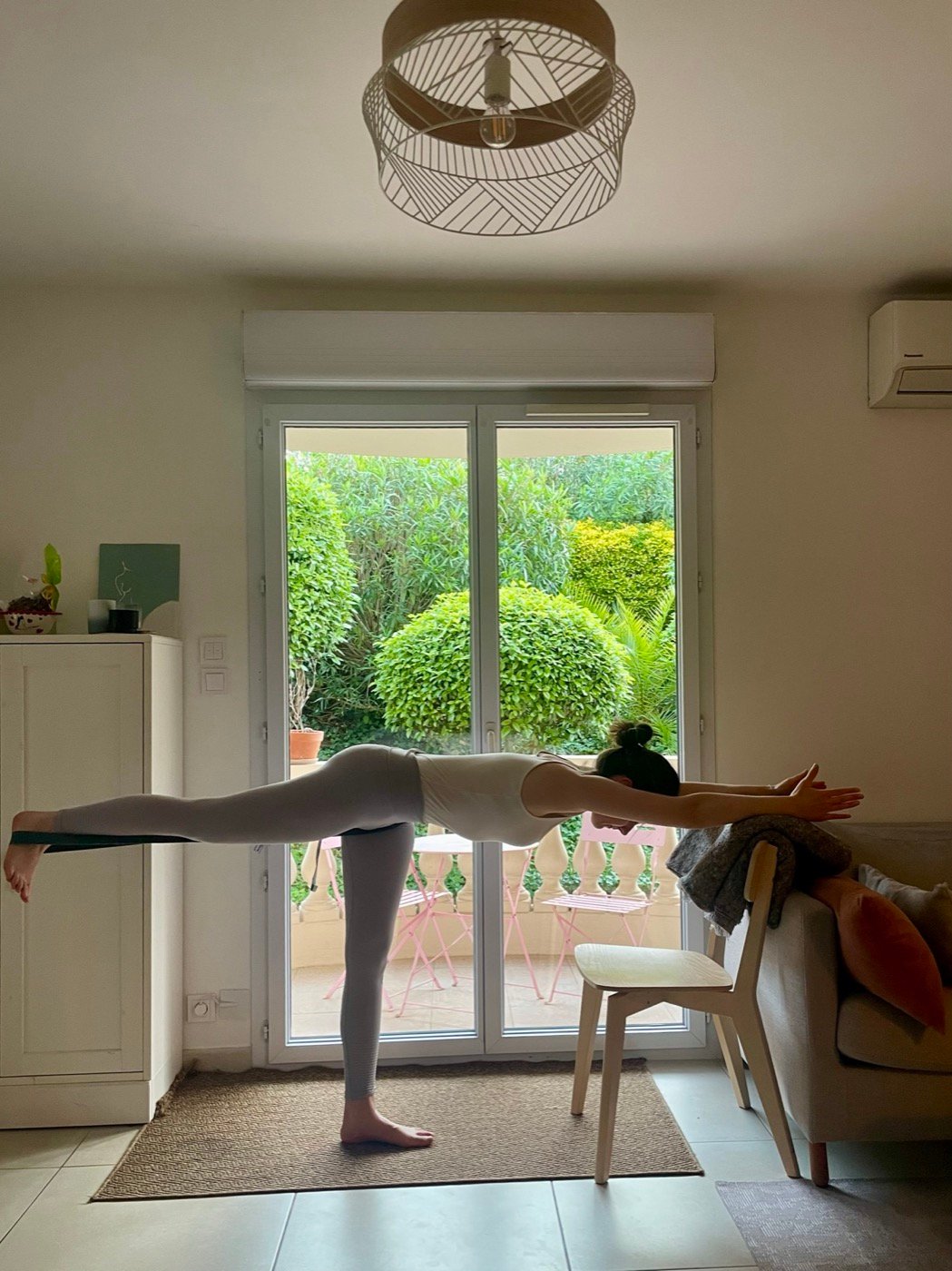 Posture du guerrier III, mains en appui sur le dossier d'une chaise